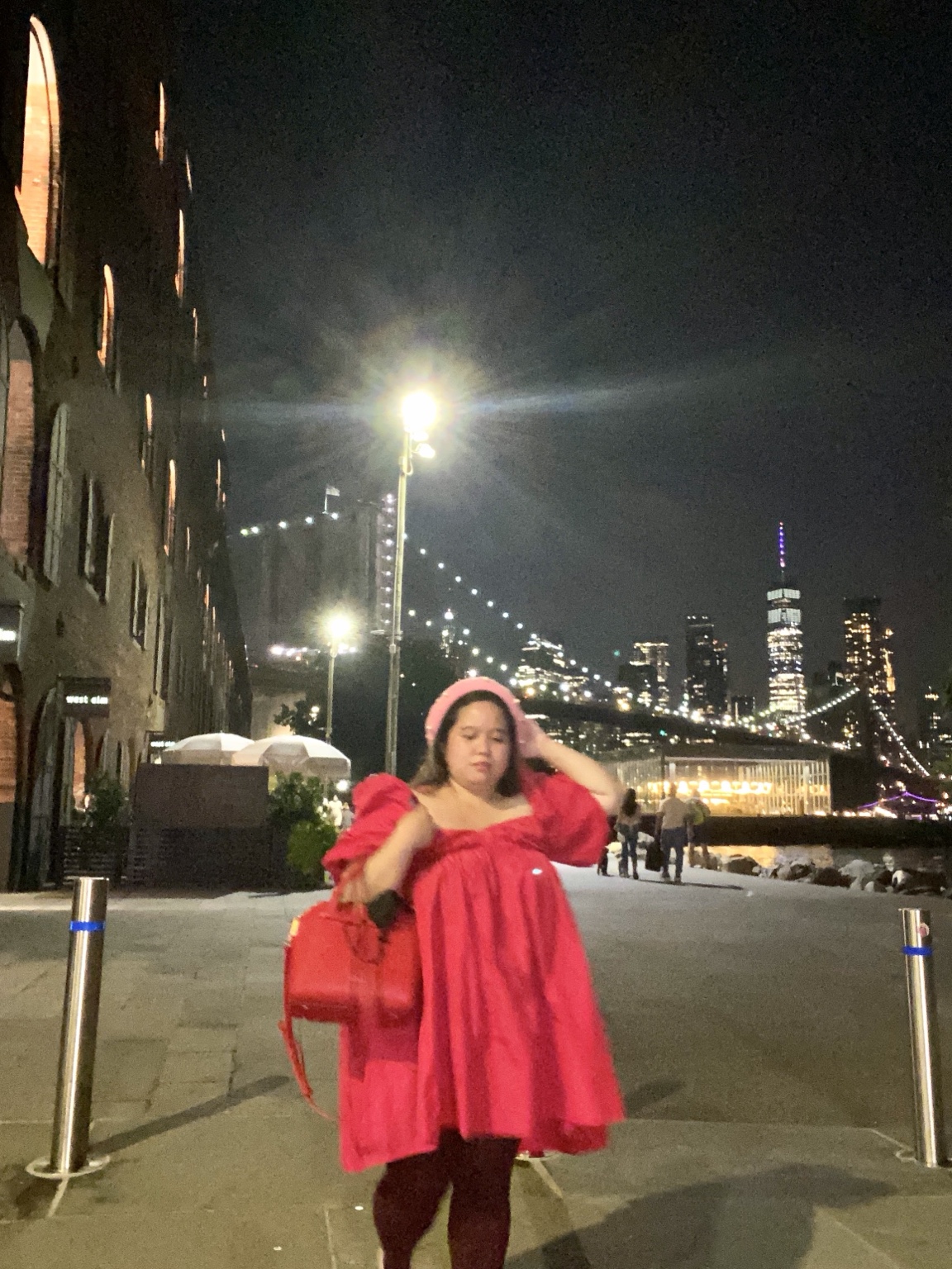 Dee in a bright red dress on a city street at night