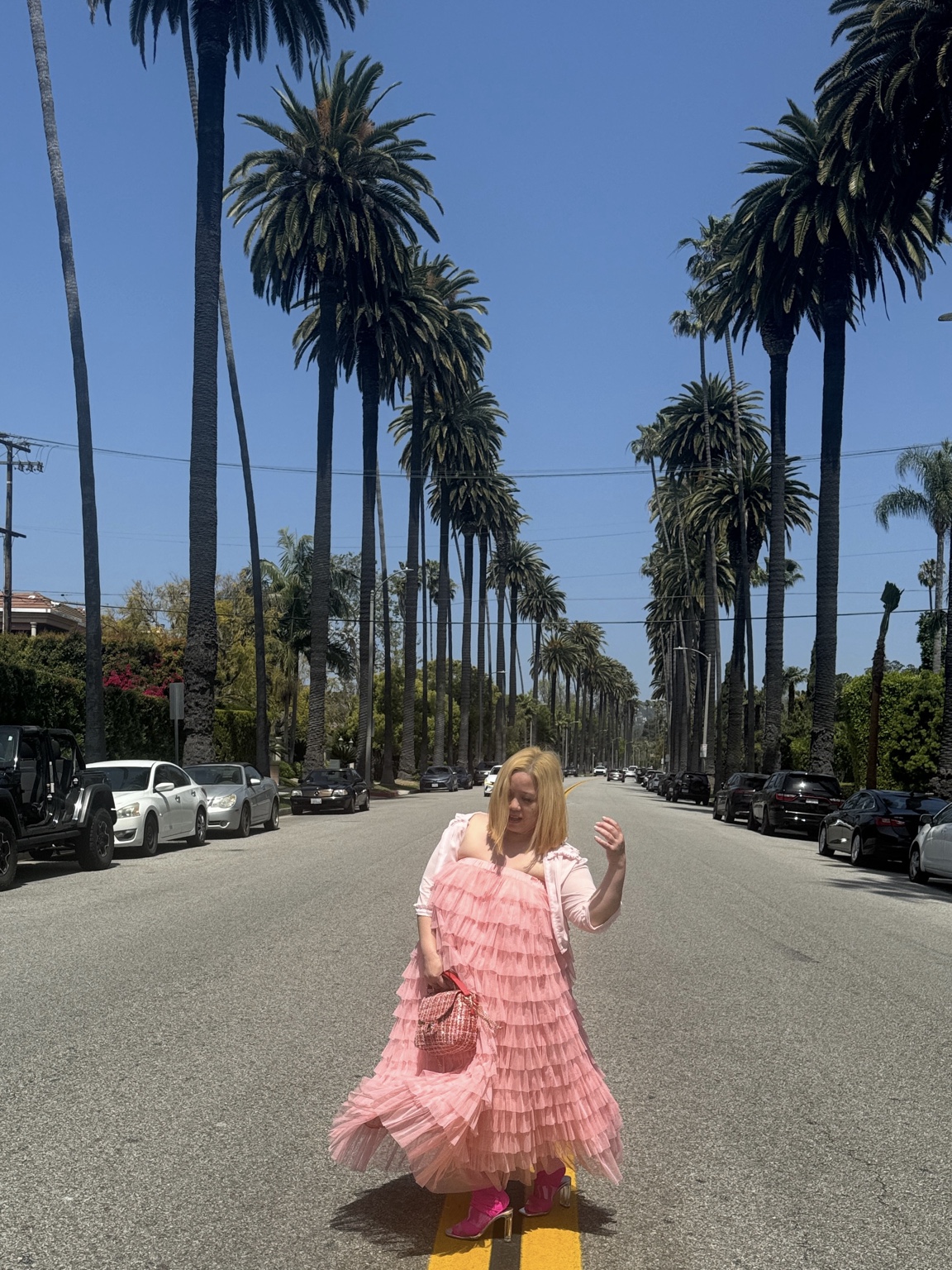 Dee in a pink dress on a palm-lined street