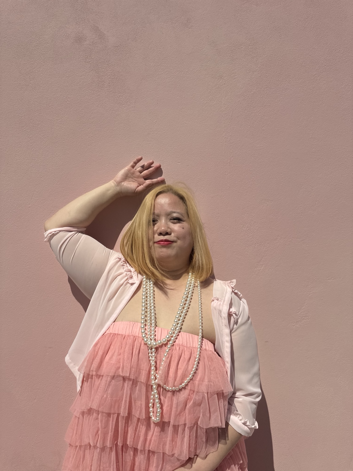 Dee wearing pearls and a pink ruffled dress with one hand raised above her head